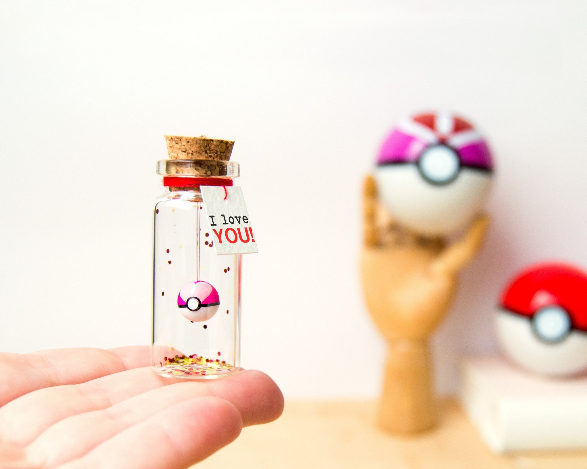 May include: A small glass bottle filled with glitter and a pink and white Pokeball charm. A tag attached to the bottle reads "I love YOU!"