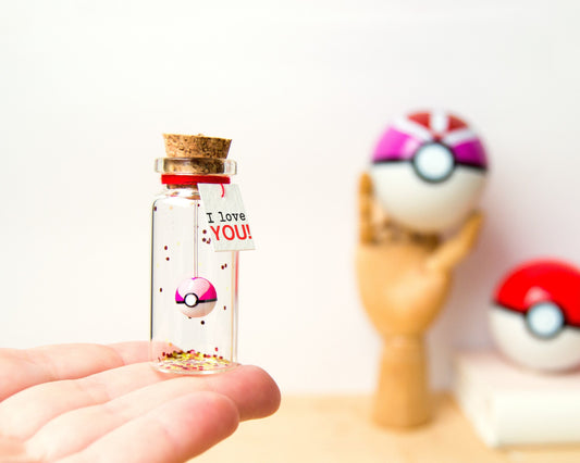 May include: A small glass bottle filled with glitter and a pink and white Pokeball charm. A tag attached to the bottle reads "I love YOU!"